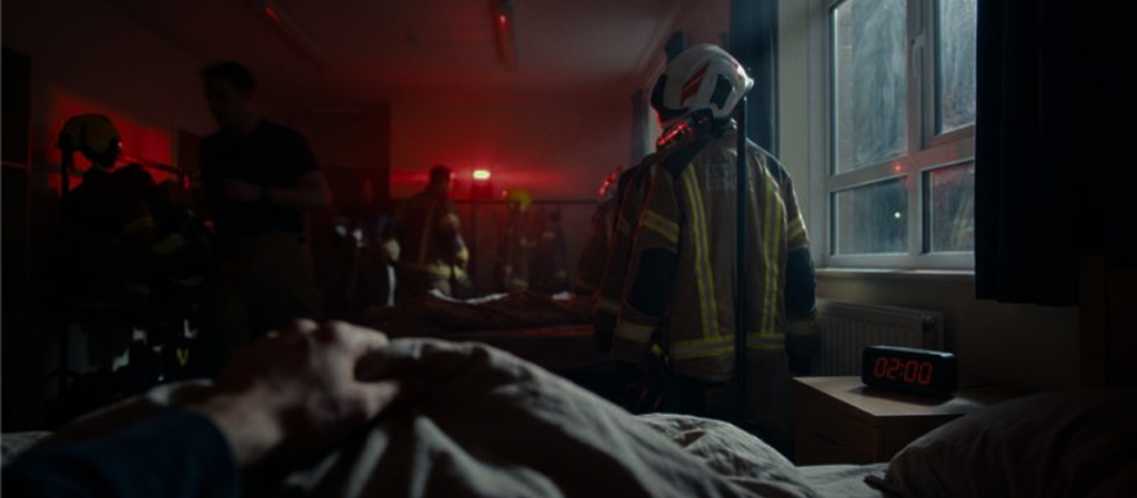 Firefighter gear stands beside bed during nighttime emergency.