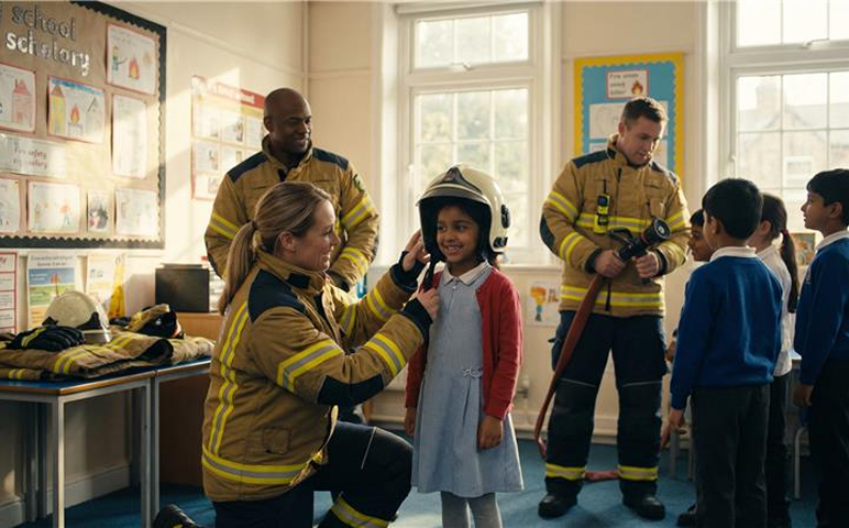 Firefighters demonstrate safety equipment to schoolchildren in classroom.