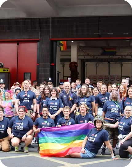 Group holding rainbow flag outside fire station Pride event.